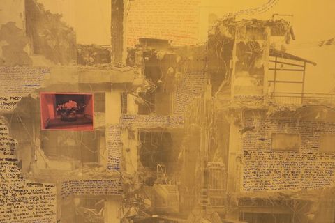 Collage. Gold-tinted black and white photographs are overlaid with areas of blue, black, and pink writing. The images are of a building that has been partially demolished so the facing wall is in ruins. A photograph of flowers in a vase, tinted coral pink, is collaged over the face of the building to our left.
